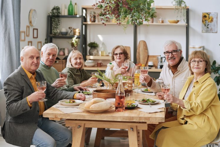 Portrait of group of old friends sitting at dining table with glasses of wine during dinner party
